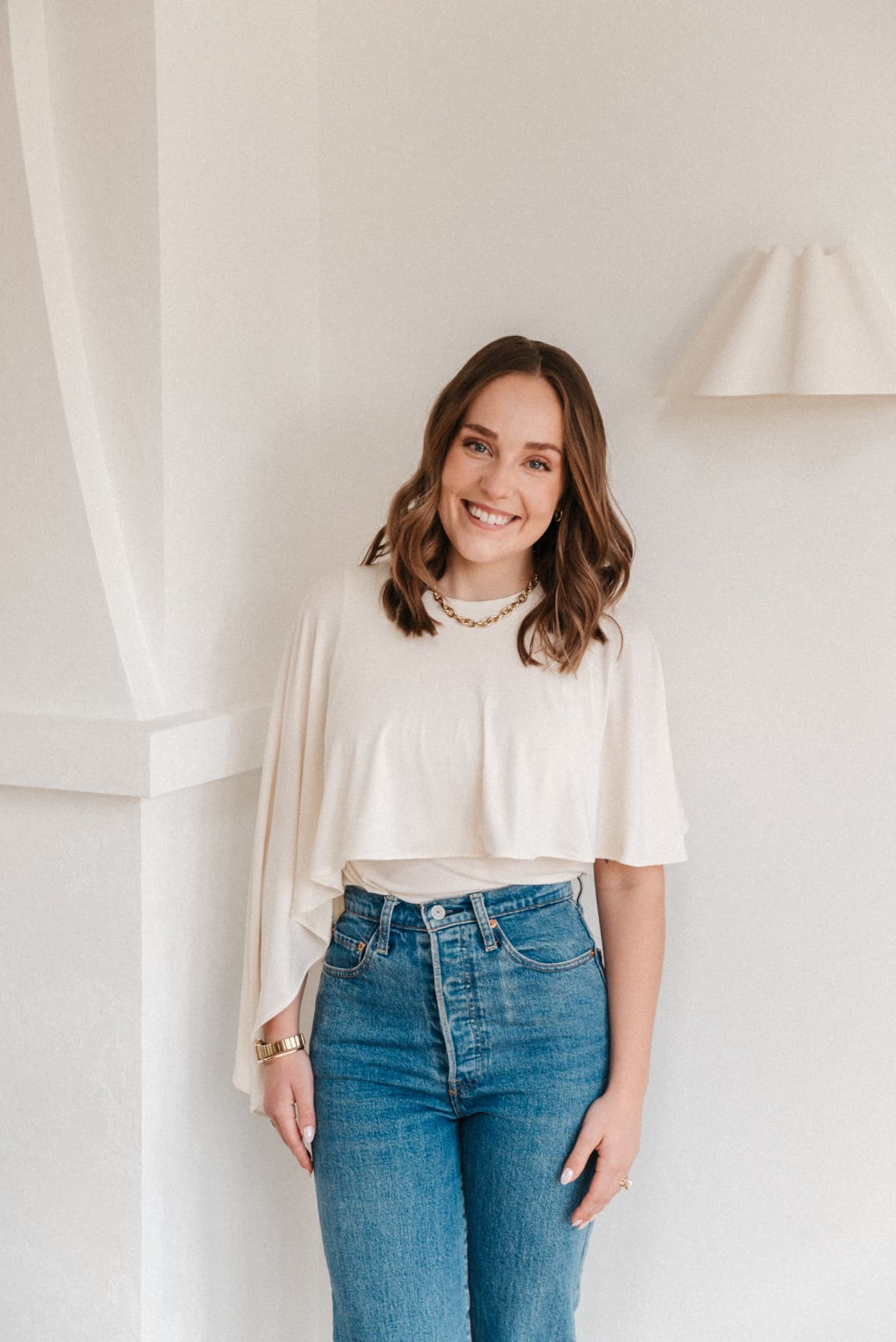 Emma, founder of STEM Creative, smiling in a bright minimal studio wearing a cream top and jeans