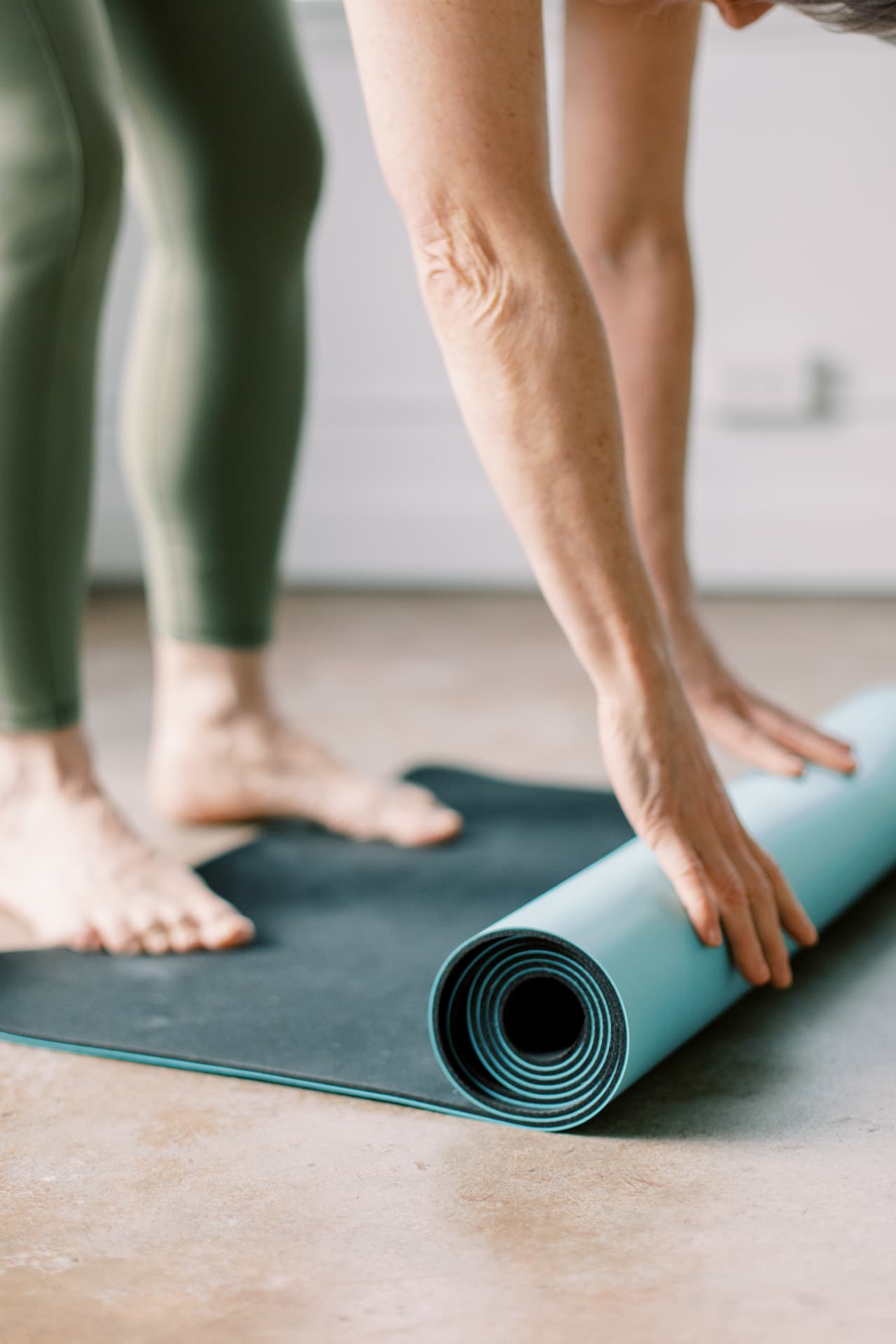 Hands rolling out a yoga mat in a bright studio, ready for movement and reset